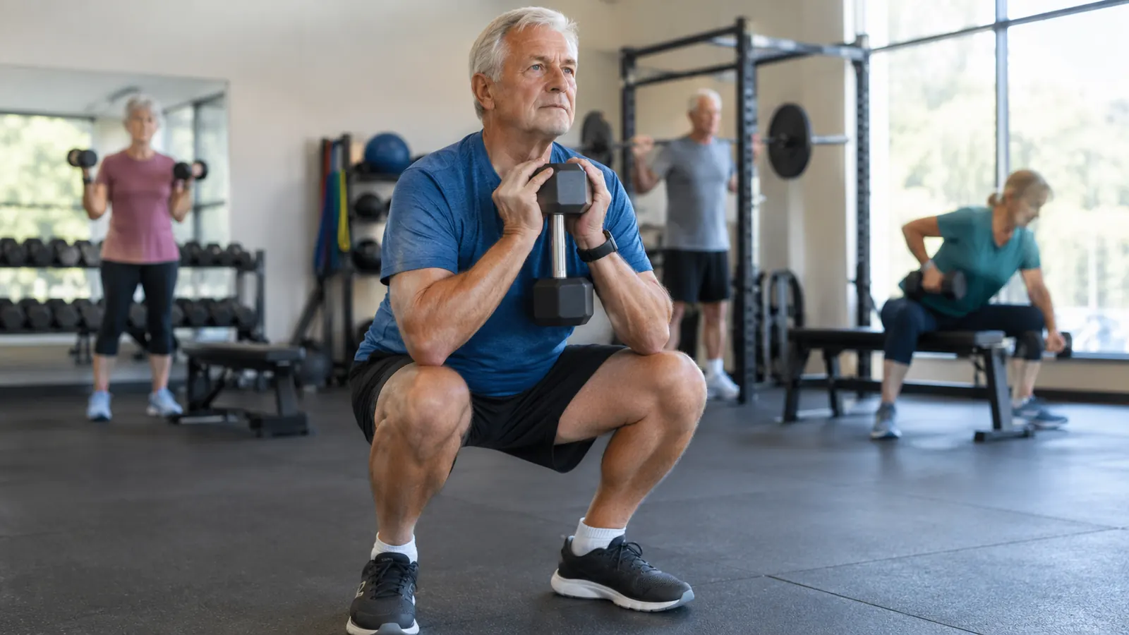 An older man in his sixties doing a goblet squat with a dumbbell at a community rec center