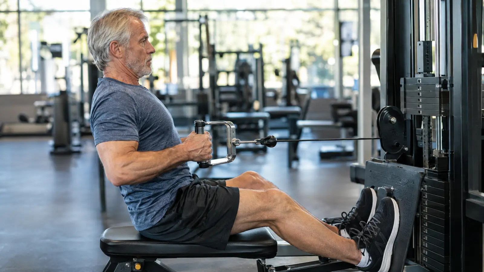 A man in his sixties doing seated rows on a cable machine at a rec center, viewed from the side